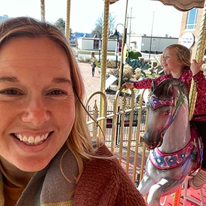 Photo of Clare H. and her daughter riding a merry go round